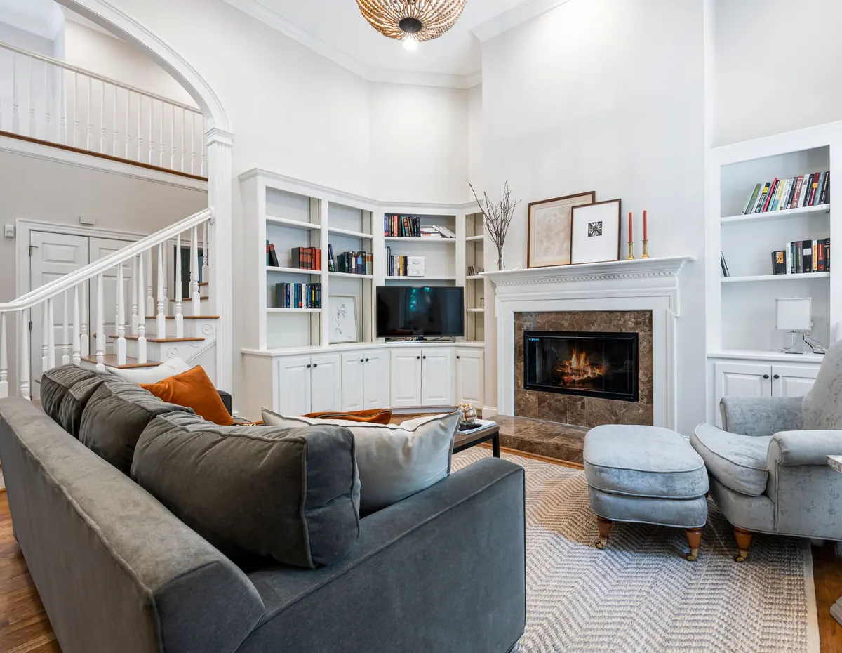 Small TV above a fireplace between white bookshelves, next to a white staircase in a two-story living room
