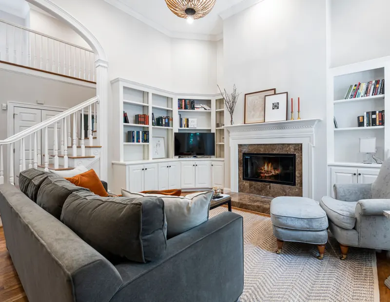 Small TV above a fireplace between white bookshelves, next to a white staircase in a two-story living room