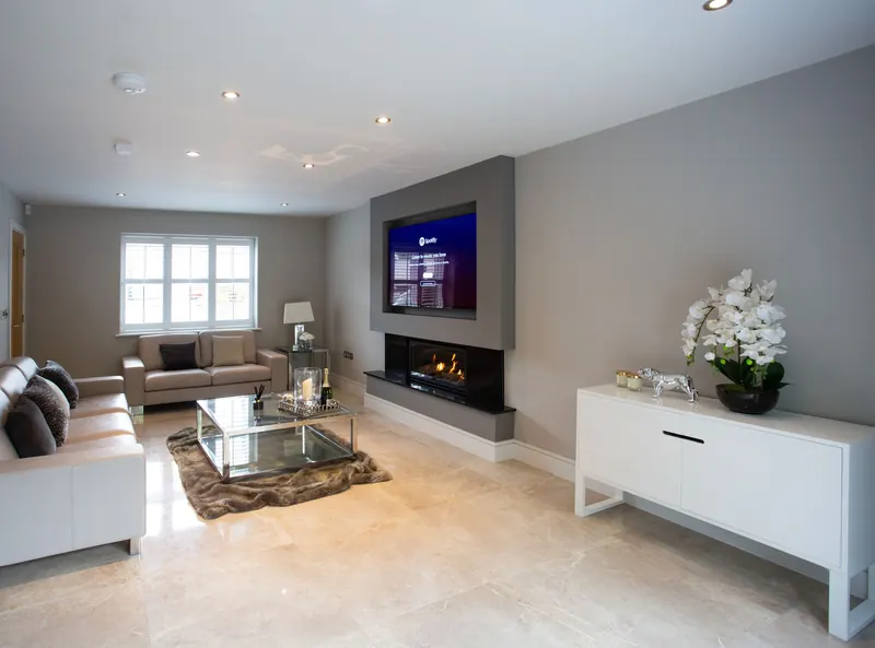 TV mounted on a grey wall above a linear fireplace in a long living room with white sofas