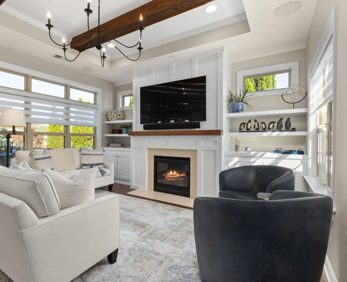 TV mounted above a fireplace between white built-in shelves, with a beamed ceiling and two armchairs in front