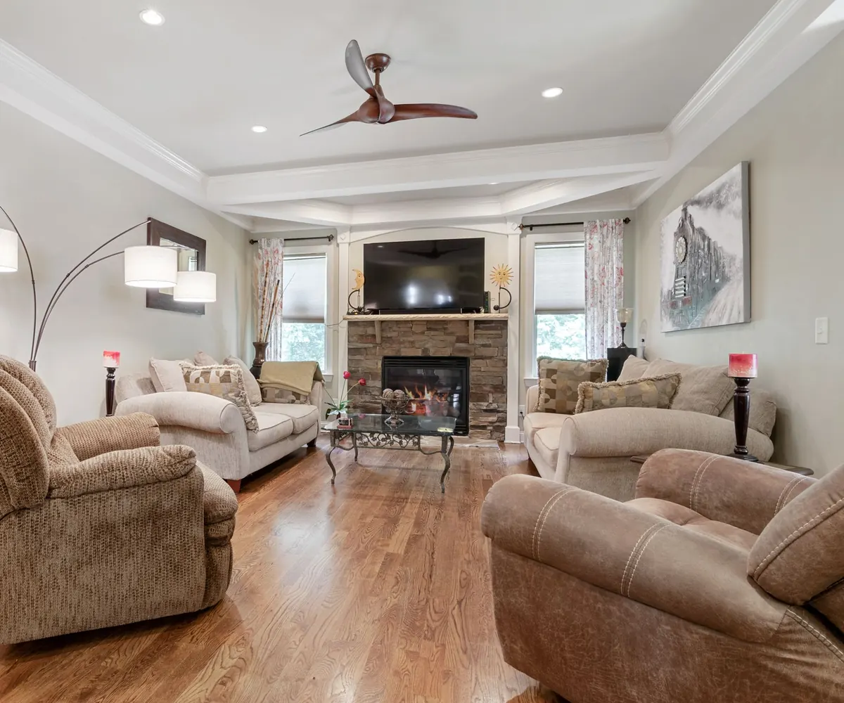 TV mounted above a stone fireplace in a bright living room with plush recliners and a ceiling fan