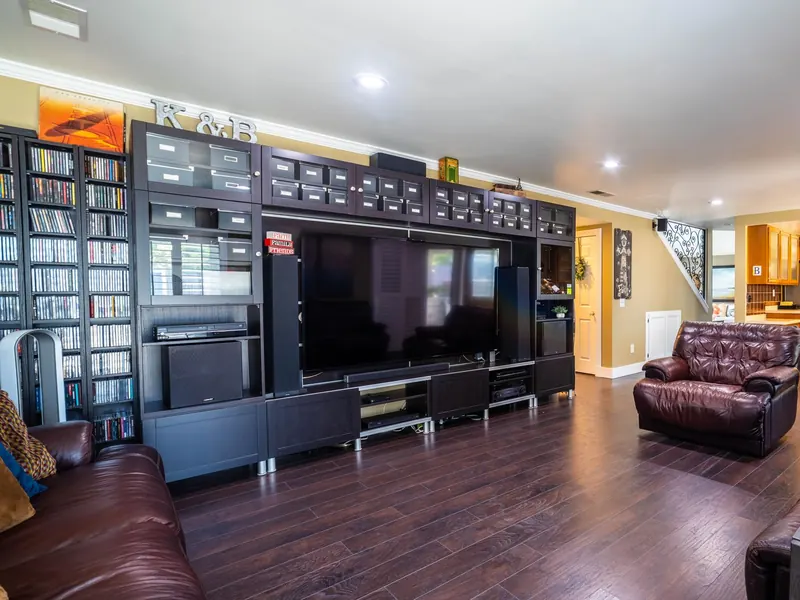 Large TV set into a dark built-in entertainment wall facing leather sofas on a wood floor