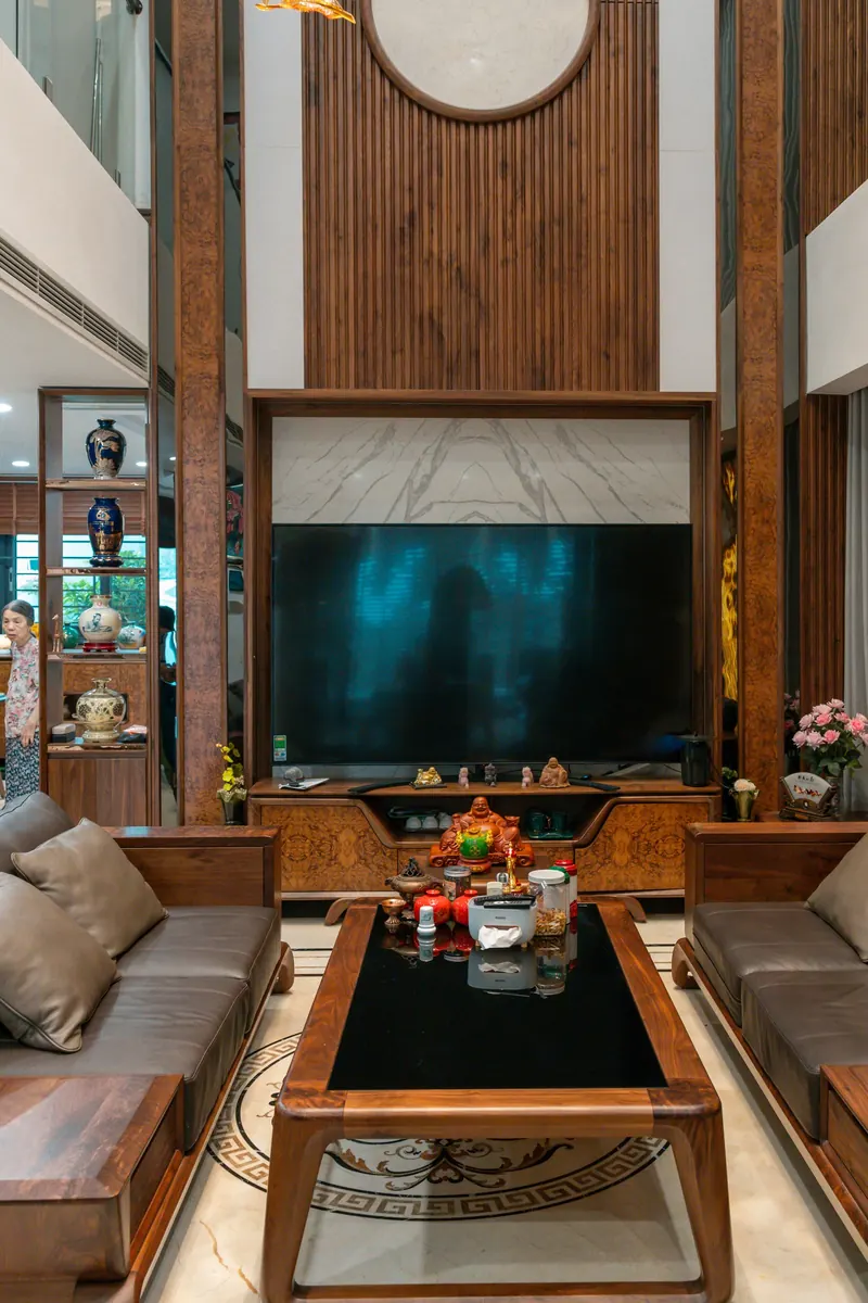 TV mounted below a tall wood slat feature wall in a double-height living room with wood sofas
