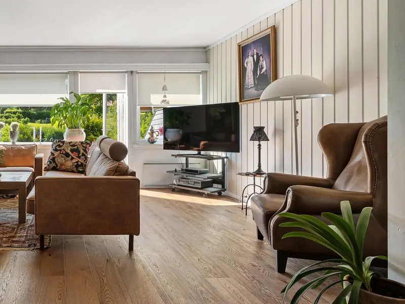 TV on a corner stand in a living room with wide wood floors, a whitewashed stone wall and leather sofas
