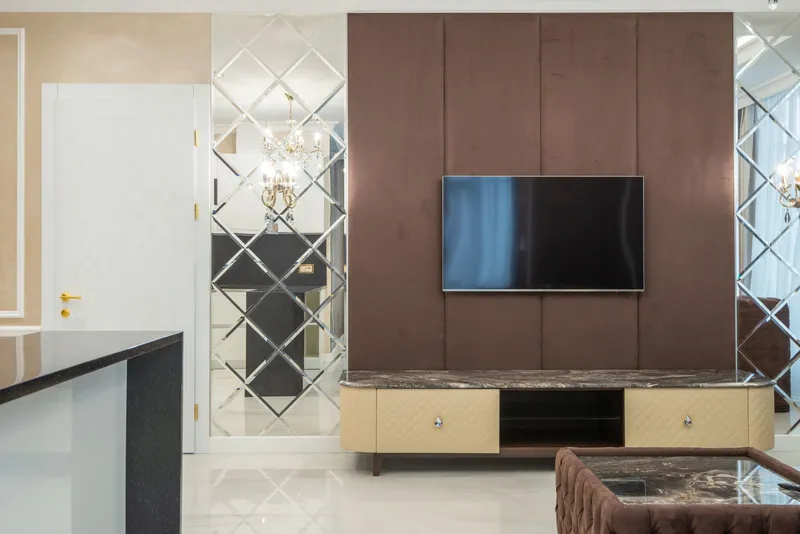 TV mounted on a brown upholstered panel wall above a cream and marble media console