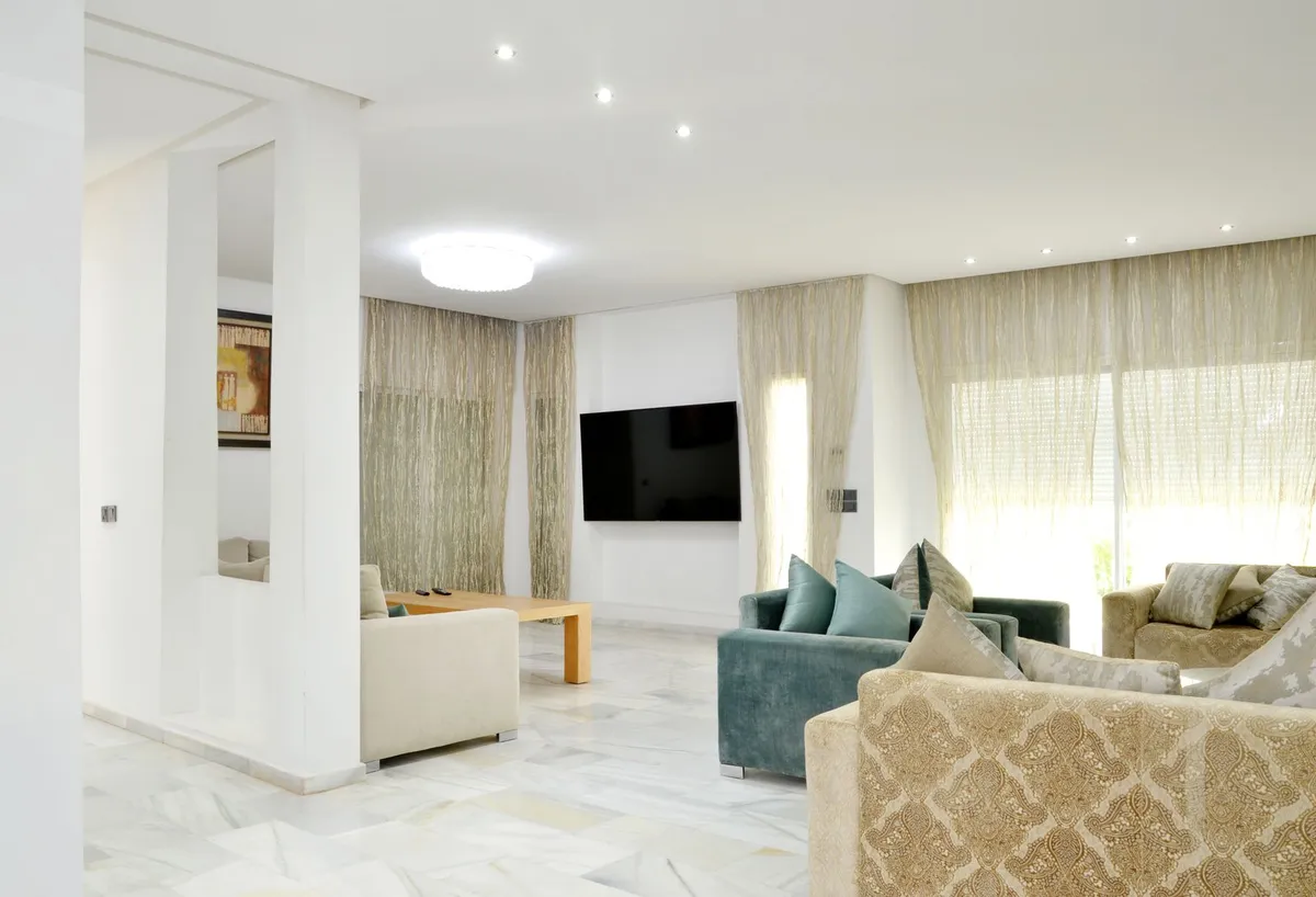 TV mounted on a white wall in a bright living room with marble floors, sheer curtains and patterned sofas